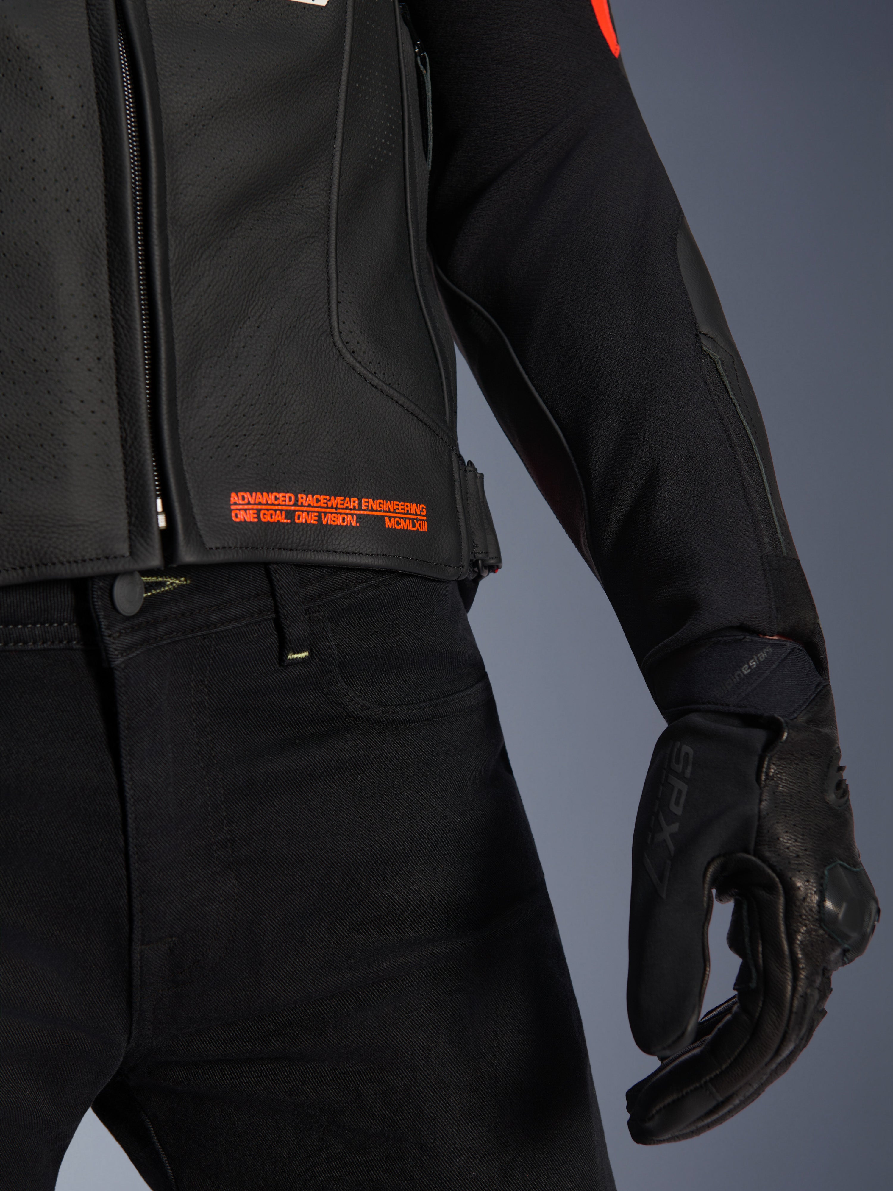 Chaqueta de cuero Alpinestars GP Plus R V4 Airflow, primer plano de la cintura y la manga, cuero perforado negro con texto en rojo flúor que dice 'Advanced Racewear Engineering', combinada con pantalones de moto negros y guante de moto SPX 7