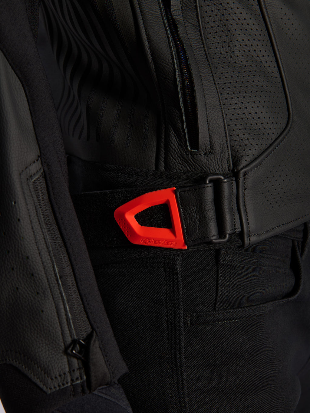 Primer plano de la chaqueta de cuero Alpinestars GP Plus R V4 Airflow, cuero negro perforado con una correa de ajuste de cintura de gancho y bucle en color rojo flúor vibrante, con un bolsillo lateral con cremallera y paneles texturizados ergonómicos.
