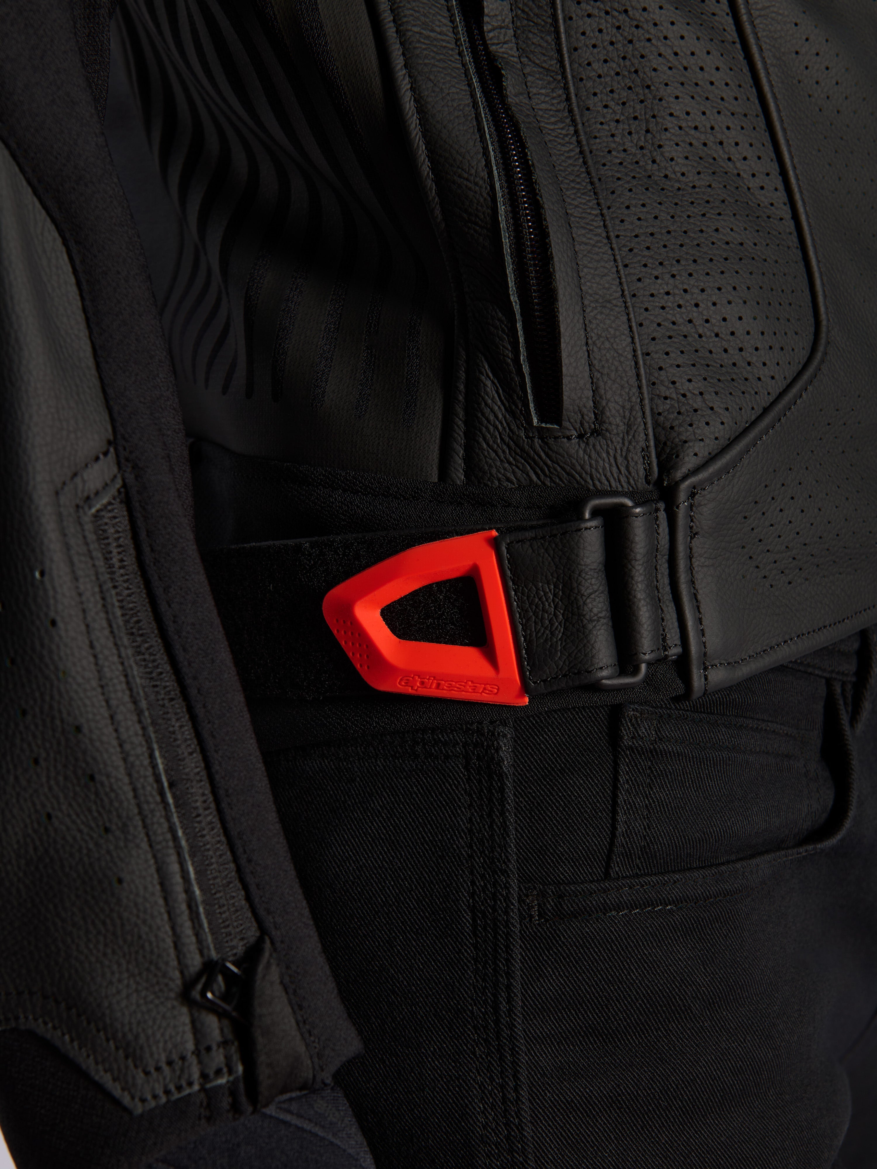 Primer plano de la chaqueta de cuero Alpinestars GP Plus R V4 Airflow, cuero negro perforado con una correa de ajuste de cintura de gancho y bucle en color rojo flúor vibrante, con un bolsillo lateral con cremallera y paneles texturizados ergonómicos.