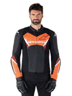 Chaqueta de cuero Alpinestars Faster V3, chaqueta deportiva para moto, negro y rojo flúor, vestida por un modelo masculino con guantes y pantalones de motorista negros, con logotipos llamativos de Alpinestars en el pecho y los antebrazos, construcción en cuero de primera calidad para conducción en carretera.