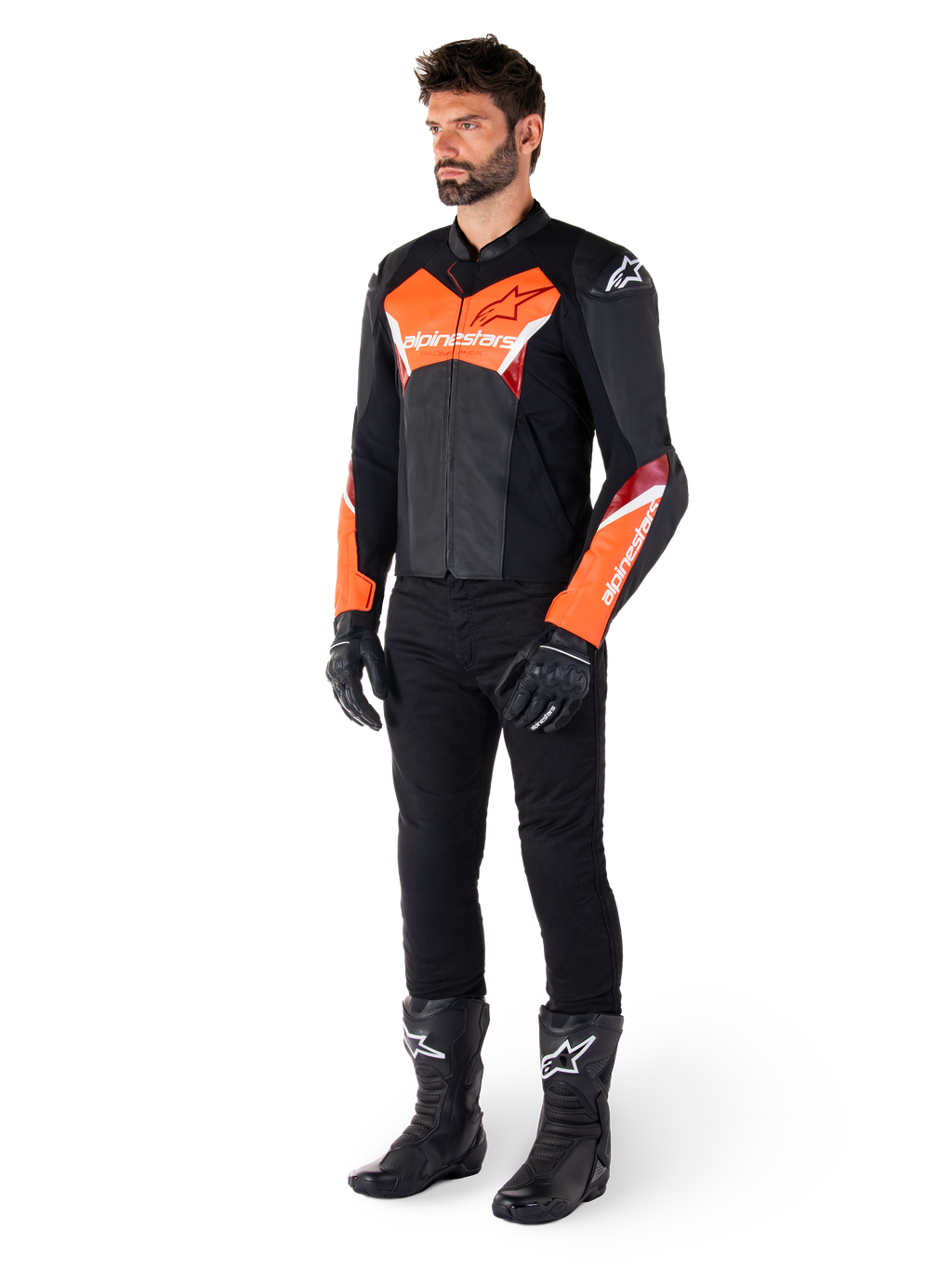 Piloto masculino con la chaqueta de cuero Alpinestars Faster V3 en negro y rojo flúor, combinada con pantalones de conducción, guantes y botas negros. La chaqueta presenta una silueta derivada de la competición con llamativos detalles en rojo flúor en el pecho y las mangas, logotipos de Alpinestars en blanco y una confección en cuero premium.