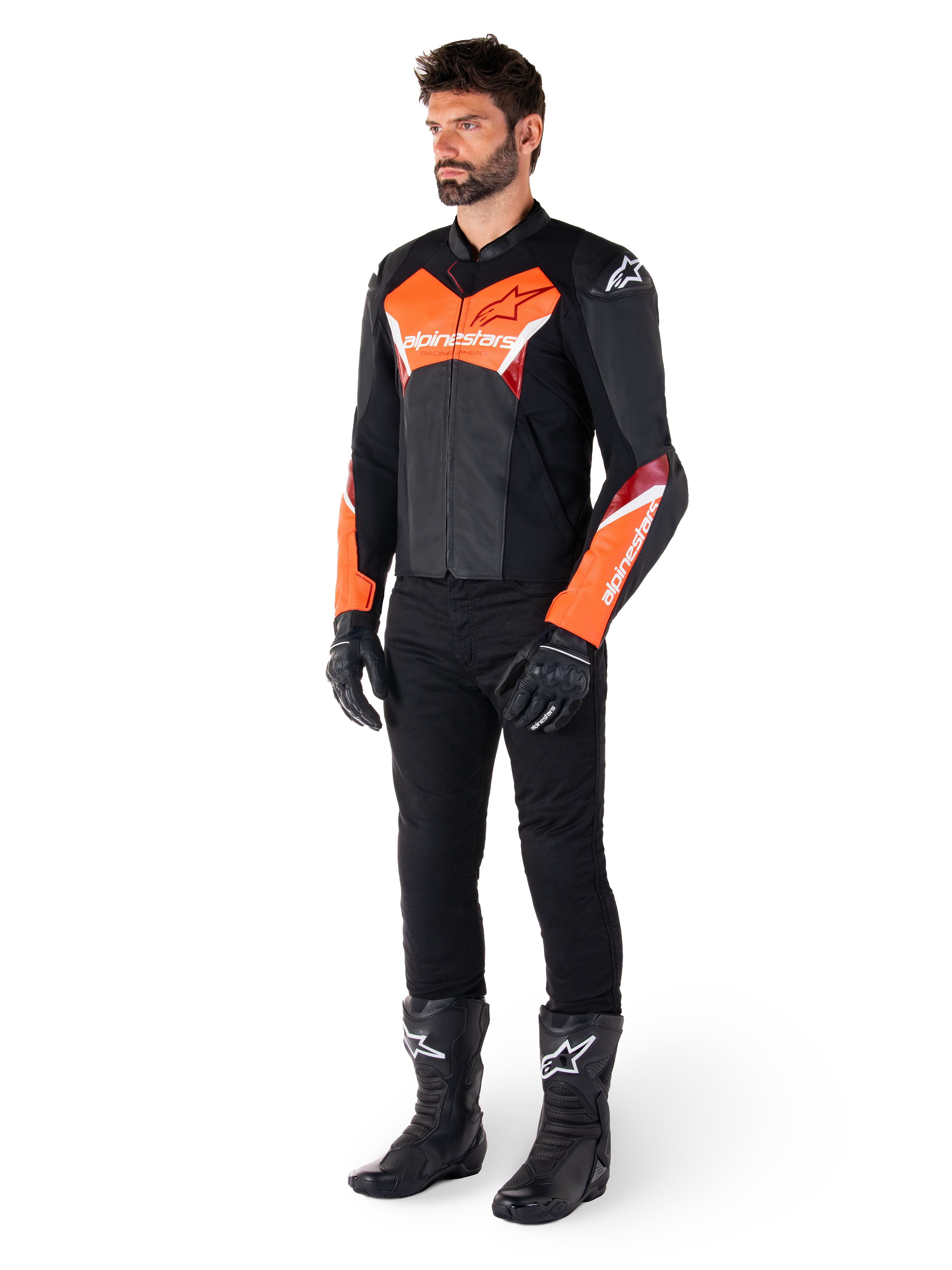 Piloto masculino con la chaqueta de cuero Alpinestars Faster V3 en negro y rojo flúor, combinada con pantalones de conducción, guantes y botas negros. La chaqueta presenta una silueta derivada de la competición con llamativos detalles en rojo flúor en el pecho y las mangas, logotipos de Alpinestars en blanco y una confección en cuero premium.