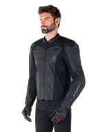 Modelo con la chaqueta de cuero Alpinestars Faster V3 Airflow en negro, chaqueta de moto deportiva con cuero perforado y paneles elásticos, combinada con pantalones negros y guantes negros con detalles rojos, estilo estilizado derivado de la competición.