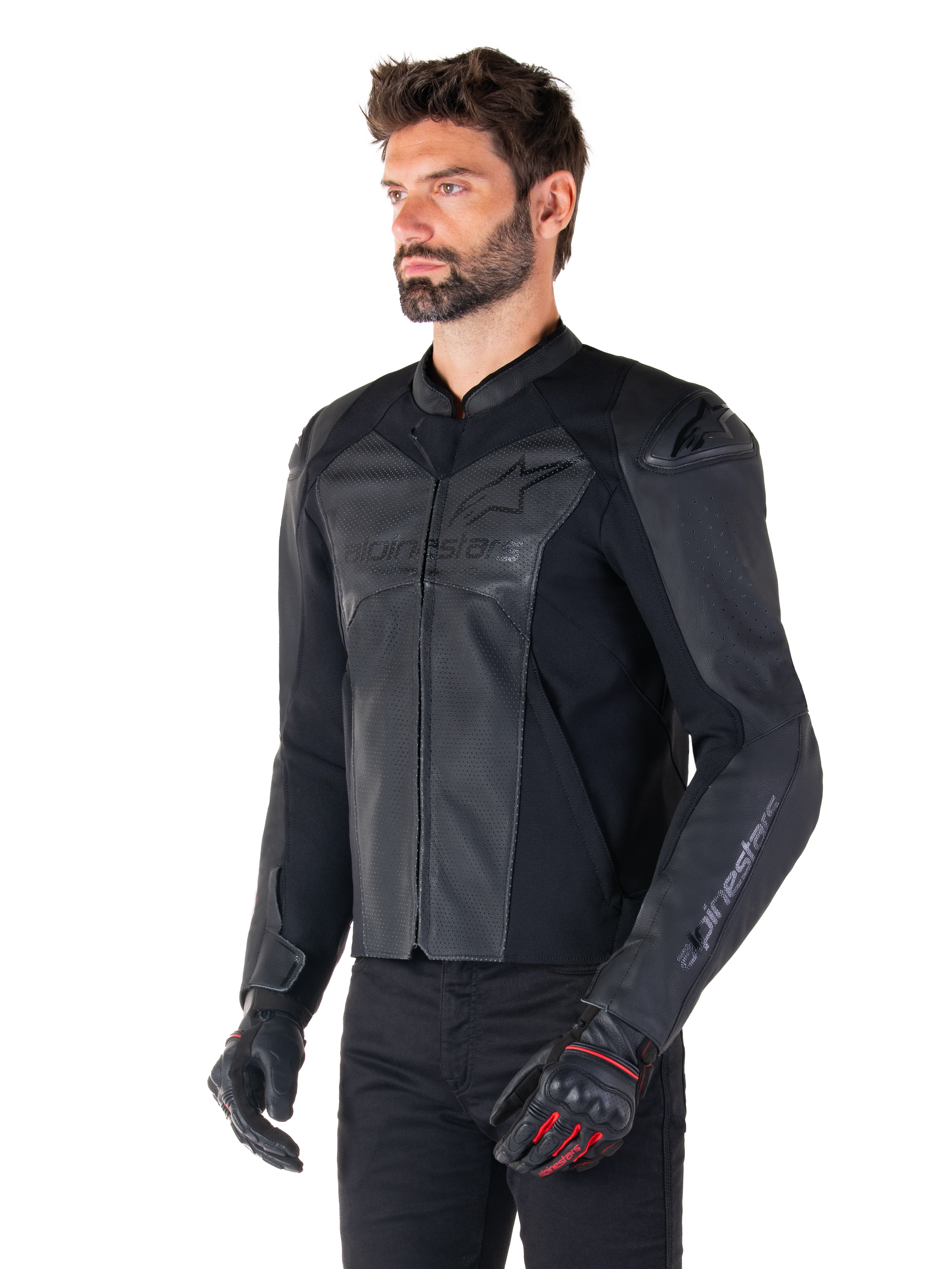 Modelo con la chaqueta de cuero Alpinestars Faster V3 Airflow en negro, chaqueta de moto deportiva con cuero perforado y paneles elásticos, combinada con pantalones negros y guantes negros con detalles rojos, estilo estilizado derivado de la competición.