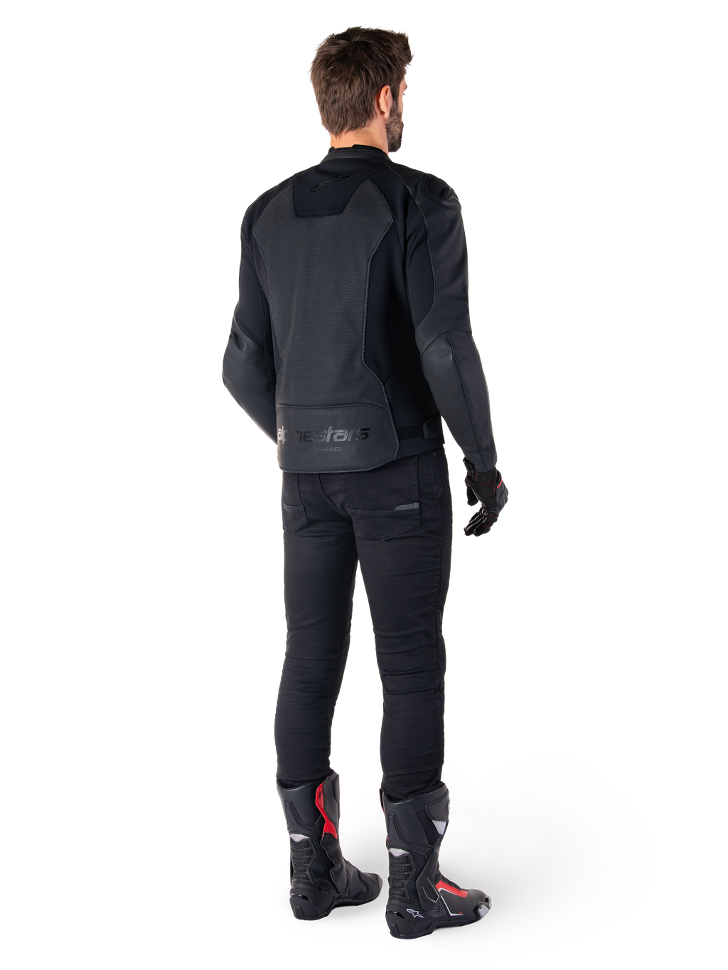 Alpinestars Faster V3 Airflow Leather Jacket, negra, vista trasera de un hombre con una chaqueta de cuero deportiva con paneles traseros perforados y marca Alpinestars, combinada con pantalones de conducción negros y botas negras y rojas.