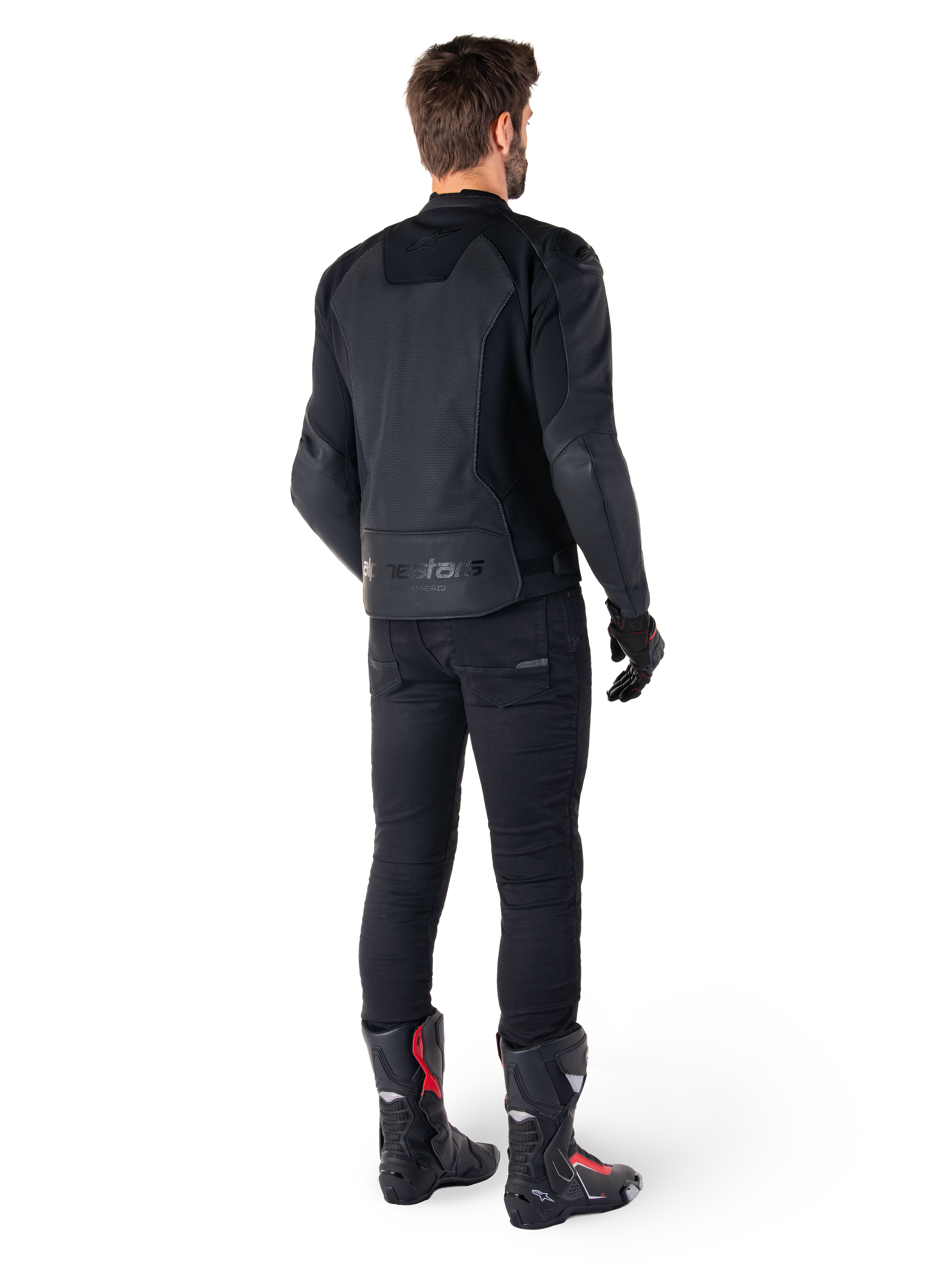 Alpinestars Faster V3 Airflow Leather Jacket, negra, vista trasera de un hombre con una chaqueta de cuero deportiva con paneles traseros perforados y marca Alpinestars, combinada con pantalones de conducción negros y botas negras y rojas.