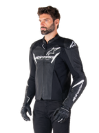 Chaqueta de cuero Alpinestars Faster V3 Airflow, negro y blanco, chaqueta deportiva para moto con paneles de cuero perforado, logotipo de Alpinestars en blanco en el pecho y los brazos, usada por un modelo con guantes y pantalones negros, equipo de conducción elegante y protector