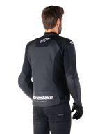Chaqueta de cuero Alpinestars Faster V3 Airflow, negro y blanco, vista posterior en un modelo, con espalda de cuero perforado para ventilación, logos Astars blancos en la parte superior de la espalda y en la parte inferior de la cintura con el texto 'Racing Ahead', diseño deportivo con paneles elásticos para motociclismo.