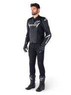 Modelo con la chaqueta de cuero Alpinestars Faster V3 Airflow, negra y blanca, con cuero perforado y logotipos Alpinestars blancos, combinada con pantalones, guantes y botas de conducción negros, equipamiento de motociclismo de estilo deportivo