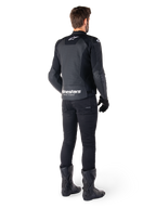 Chaqueta de cuero Alpinestars Faster V3 Airflow, negro y blanco, vista posterior que muestra los paneles de cuero perforados y el logotipo de Alpinestars en la parte baja de la espalda, vestida por un piloto con pantalones, guantes y botas de motorista negros.