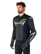 Chaqueta de cuero Alpinestars Faster V3 Airflow, chaqueta de moto deportiva, negro, blanco y amarillo flúor, usada por un hombre, con cuero perforado para el flujo de aire, logotipos de Alpinestars en el pecho y los brazos, combinada con guantes negros.