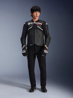 Modelo con la chaqueta de cuero Alpinestars Atem V5 en negro y blanco, con la marca Alpinestars en blanco y un logotipo de estrella roja en el pecho, combinada con pantalones negros y guantes de carreras en blanco y negro, equipamiento de motociclismo de alto rendimiento