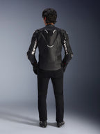 Chaqueta de cuero Alpinestars Atem V5, chaqueta de carreras para moto, negra y blanca, vista trasera sobre el piloto, con joroba aerodinámica y marca Alpinestars en blanco en las mangas y la espalda, construcción técnica de cuero, usada con pantalones negros y botas de conducción