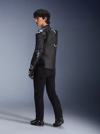 Modelo masculino con la chaqueta de cuero Alpinestars Atem V5 en negro y blanco, vista trasera de tres cuartos que muestra la joroba aerodinámica y los protectores DFS RR, combinada con pantalones negros, guantes de carreras y botas, equipamiento profesional de motociclismo