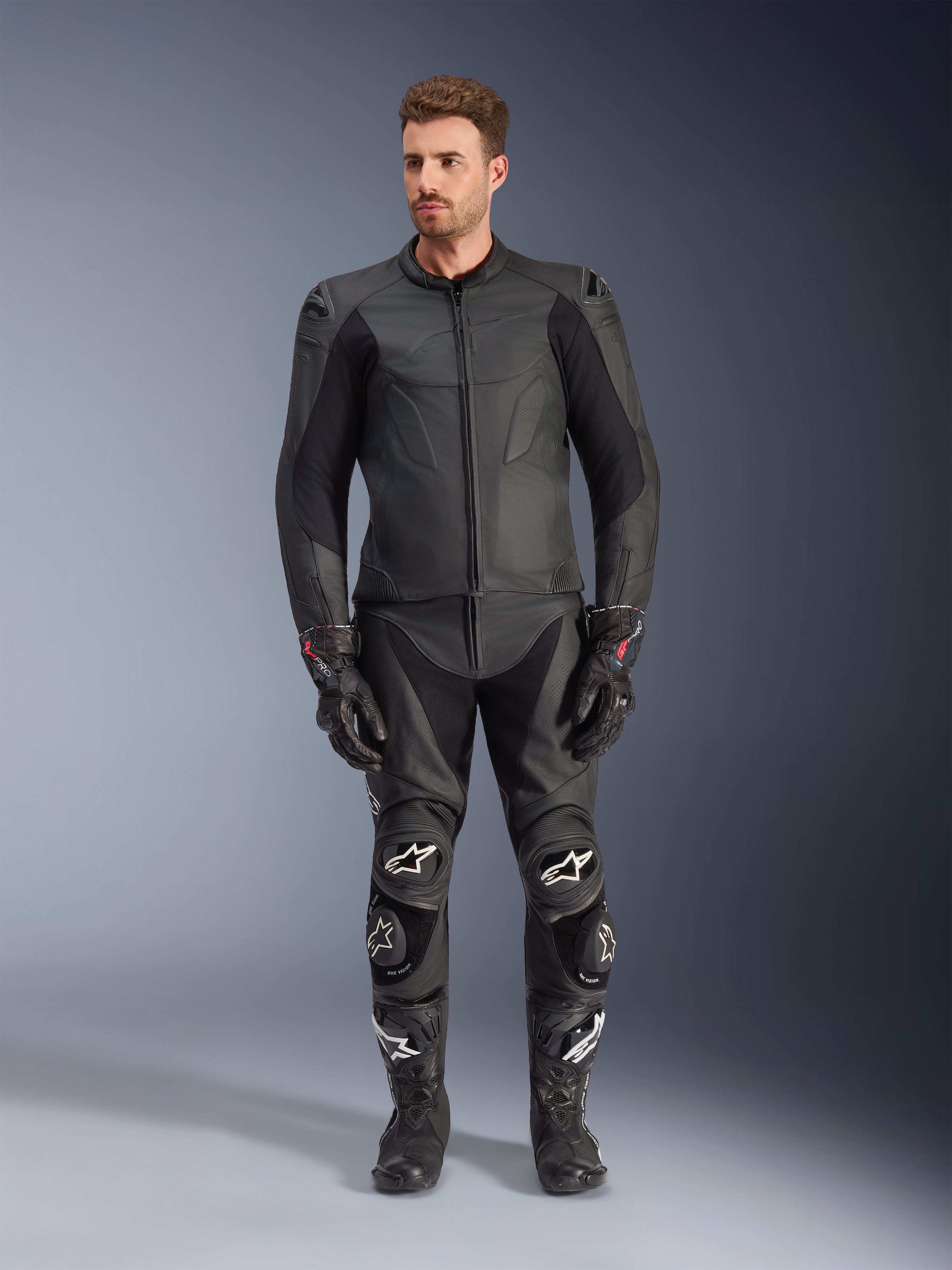 Chaqueta de cuero Alpinestars Caliber, chaqueta de moto negra, combinada con pantalones de carreras, guantes y botas a juego, con un diseño elegante con logotipos en el mismo tono, paneles elásticos en las mangas y deslizadores protectores en los hombros, en un entorno de estudio profesional