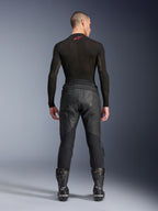 Alpinestars Missile V3 Leather Pants, negros, vista posterior en un modelo con camiseta de compresión de manga larga y botas de carreras, confección en cuero de primera calidad con superposición en la cintura alta y zonas elásticas, equipamiento profesional para carreras de motos