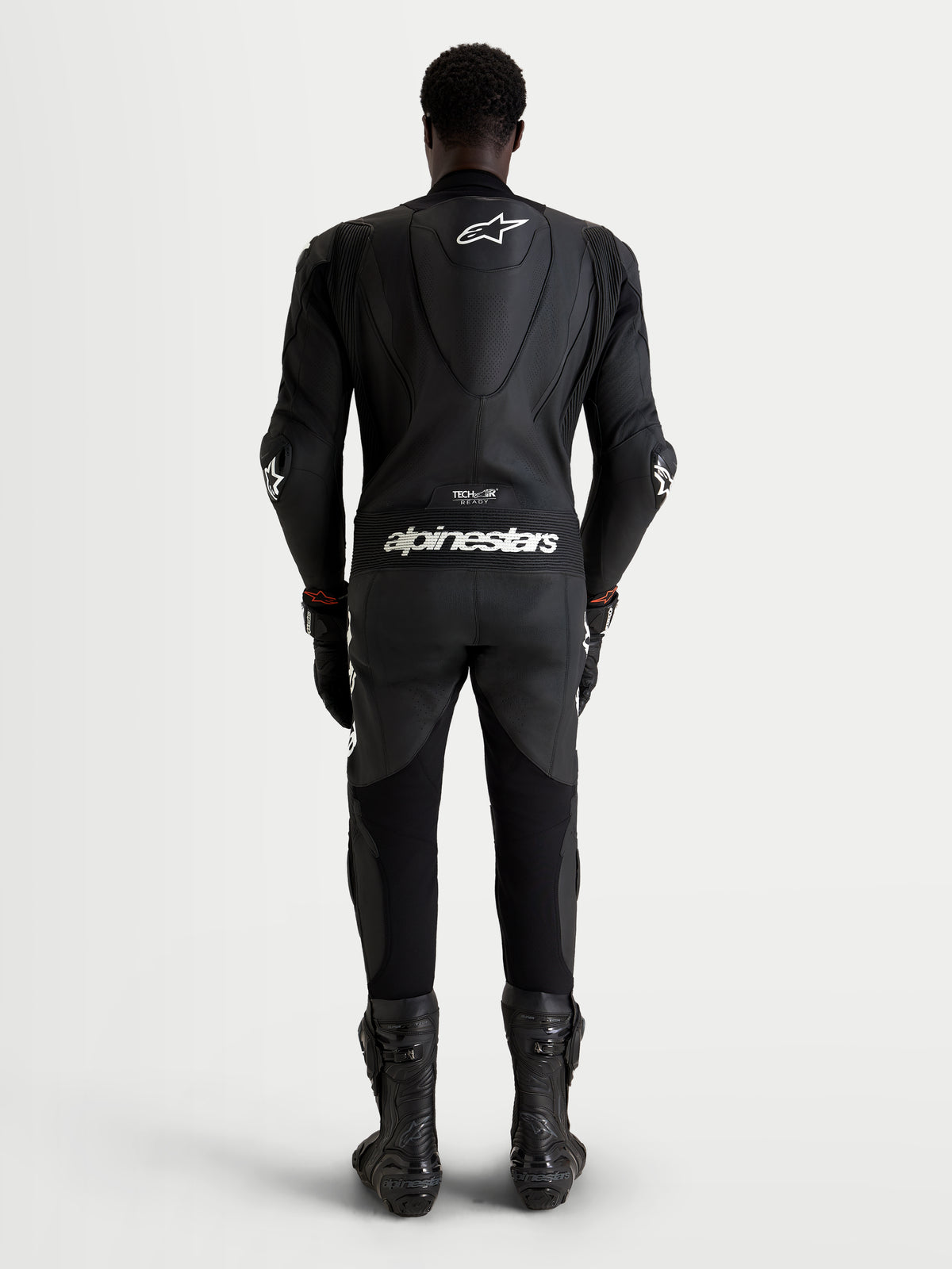Alpinestars Missile V3 Leather Suit 1 Pc, mono de cuero de una pieza para moto de carreras, negro con logotipos blancos, vista trasera de un piloto