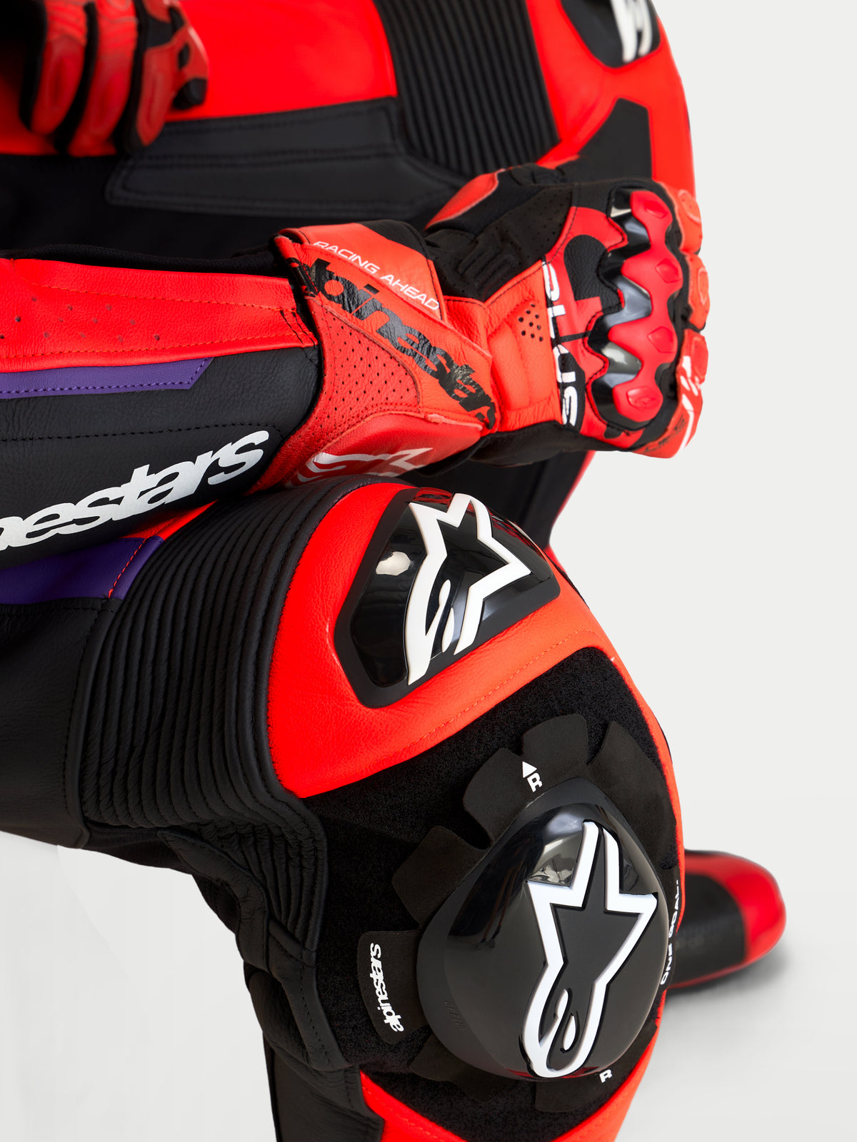 Alpinestars Missile V3, mono de cuero de una pieza para moto, negro, rojo y morado, detalle en primer plano de la rodillera y el guante con protecciones integradas