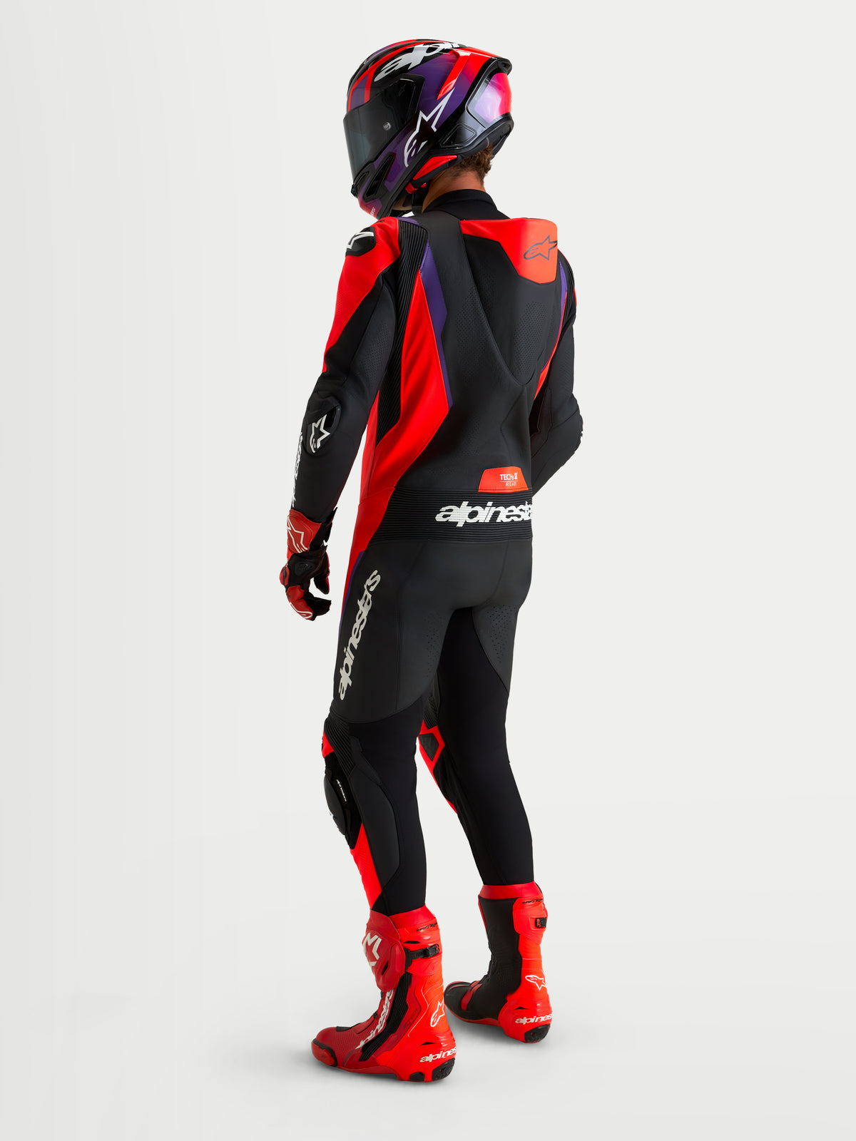 Alpinestars Missile V3, mono de cuero de una pieza para moto de carreras, negro, rojo flúor y morado, con joroba aerodinámica, visto desde atrás en modelo