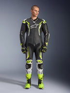 Alpinestars GP Tech V5 One Piece Leather Suit, mono de carreras profesional para motociclismo en negro y amarillo neón flúor con detalles blancos, vestido por un modelo con guantes y botas de carreras a juego, con un diseño aerodinámico y deslizadores de protección.