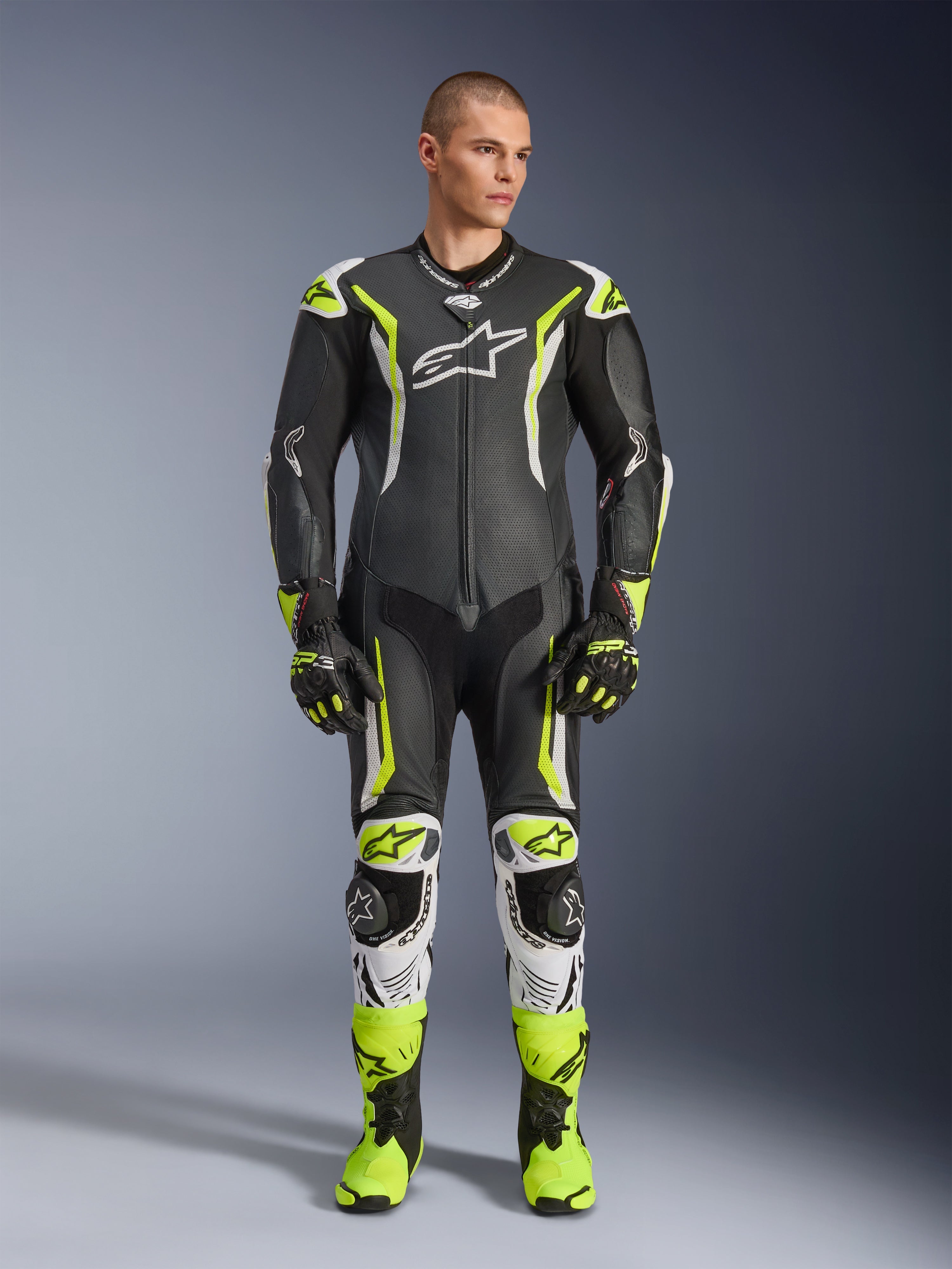 Alpinestars GP Tech V5 One Piece Leather Suit, mono de carreras profesional para motociclismo en negro y amarillo neón flúor con detalles blancos, vestido por un modelo con guantes y botas de carreras a juego, con un diseño aerodinámico y deslizadores de protección.