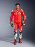 Alpinestars GP Tech V5 One Piece Leather Suit, mono de carreras profesional en rojo flúor y rojo brillante con detalles blancos, usado por un piloto con botas y guantes a juego, con joroba aerodinámica, confección en cuero de primera calidad y protecciones avanzadas para rendimiento en pista.