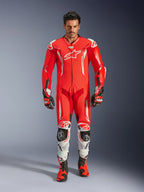 Alpinestars GP Tech V5 One Piece Leather Suit, mono de carreras profesional en rojo flúor y rojo brillante con detalles blancos, usado por un piloto con botas y guantes a juego, con joroba aerodinámica, confección en cuero de primera calidad y protecciones avanzadas para rendimiento en pista.