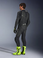 Alpinestars GP Force V2 Leather Suit, 1-Piece Black motorcycle racing suit, rear view showing aerodynamic speed hump and perforated leather, worn with neon yellow racing boots and black gloves, professional track-ready equipment