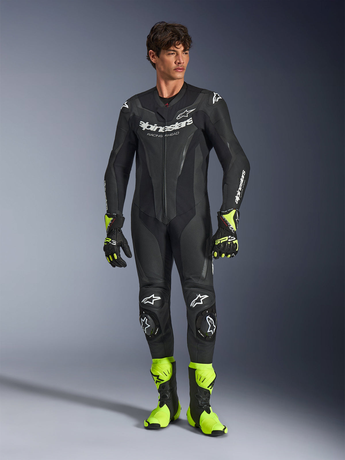 Mono de cuero Alpinestars GP Force V2, traje de motociclismo de una pieza negro, usado con botas y guantes amarillo fluorescente, con logotipos blancos y cuero perforado, diseño ajustado para días de pista