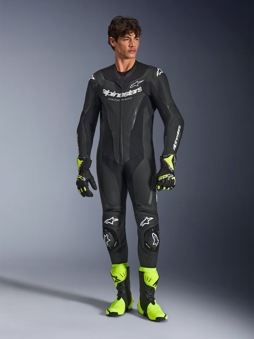 Mono de cuero Alpinestars GP Force V2, traje de motociclismo de una pieza negro, usado con botas y guantes amarillo fluorescente, con logotipos blancos y cuero perforado, diseño ajustado para días de pista