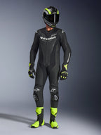 Motorcycle rider wearing the Alpinestars GP Force V2 Leather Suit in Black, 1-piece leather suit with white branding, paired with a black and fluo yellow racing helmet, gloves, and boots, professional track gear on a grey studio background