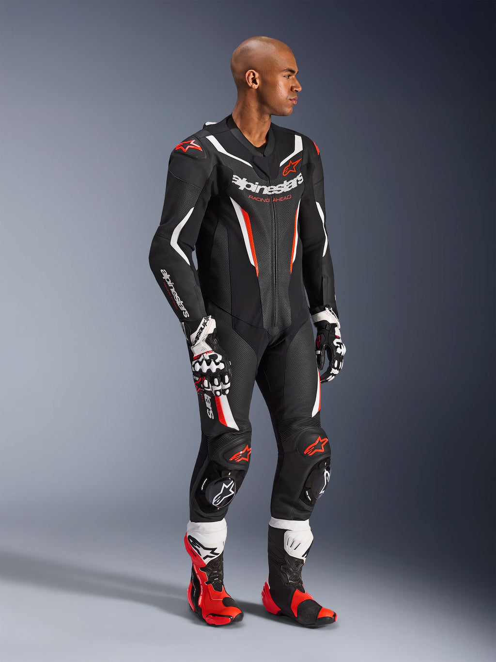 Modelo con el traje de cuero de 1 pieza Alpinestars GP Force V2 en negro, blanco y rojo flúor, equipo de competición de alto rendimiento con paneles de cuero perforado y protecciones DFS Lite, combinado con botas y guantes de carreras a juego en rojo y blanco, estética profesional de motociclismo.