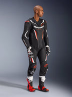 Modelo con el traje de cuero de 1 pieza Alpinestars GP Force V2 en negro, blanco y rojo flúor, equipo de competición de alto rendimiento con paneles de cuero perforado y protecciones DFS Lite, combinado con botas y guantes de carreras a juego en rojo y blanco, estética profesional de motociclismo.