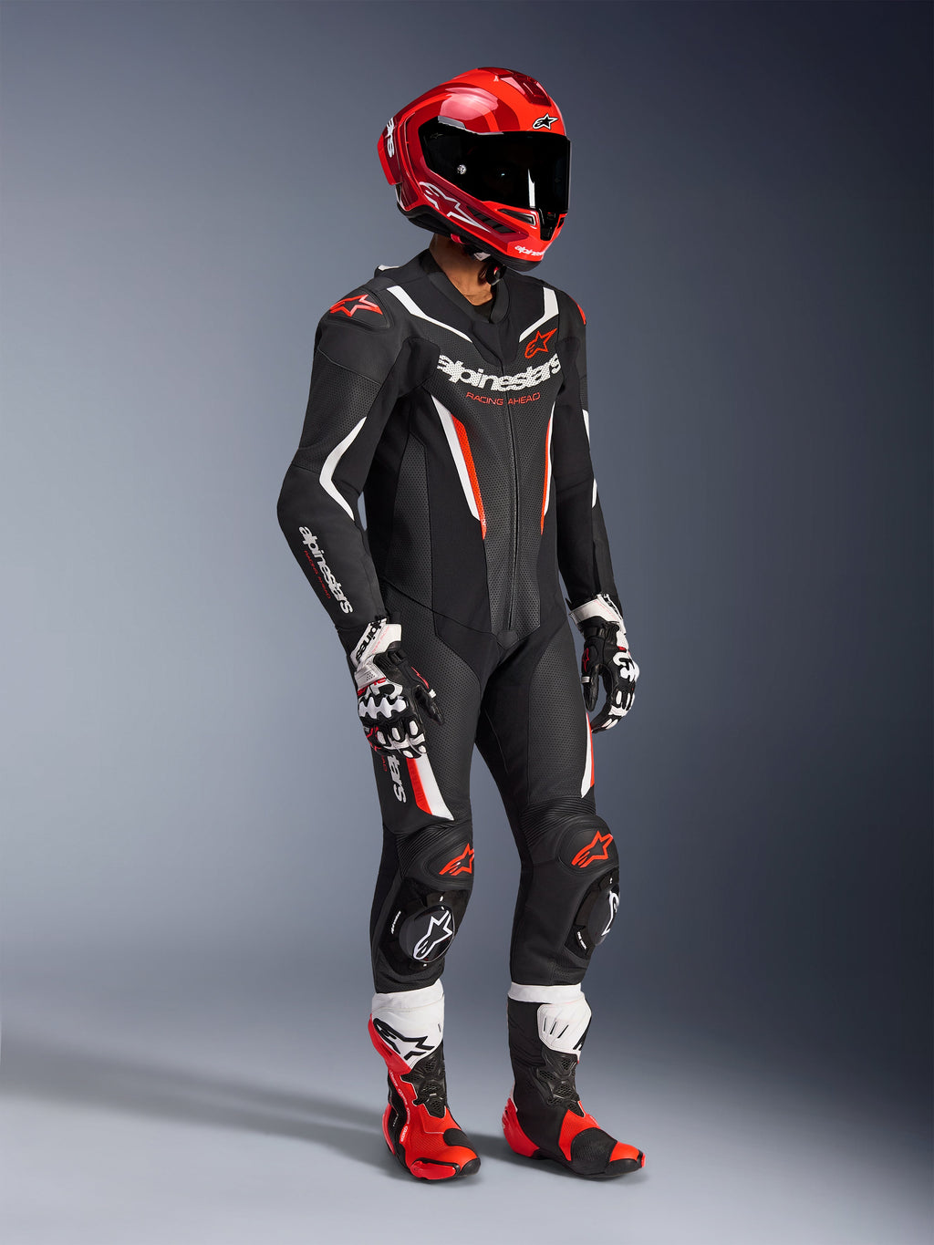 Traje de cuero Alpinestars GP Force V2 de 1 pieza, traje de carreras profesional en negro, blanco y rojo flúor, con paneles de cuero perforado y escudos DFS Lite. Equipamiento completo de pista con casco de carreras rojo, guantes y botas a juego.