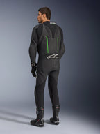 Traje de cuero Alpinestars GP Force V2, mono de motociclismo de una pieza, negro con detalles en verde, vista trasera que muestra la joroba aerodinámica y el logotipo blanco en el panel elástico de acordeón, combinado con botas y guantes de carreras negros.