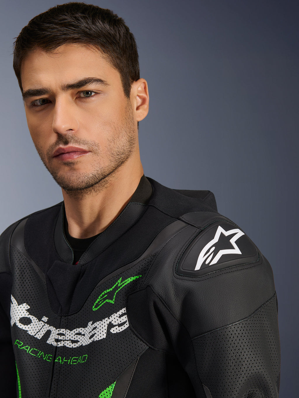 Alpinestars GP Force V2 Leather Suit - 1 Pieza, negro y verde, primer plano de un modelo masculino con el traje de carreras de motociclismo, con logotipos en blanco y verde, paneles de cuero perforado y protección de hombro DFS Lite con el logotipo de la estrella blanca.