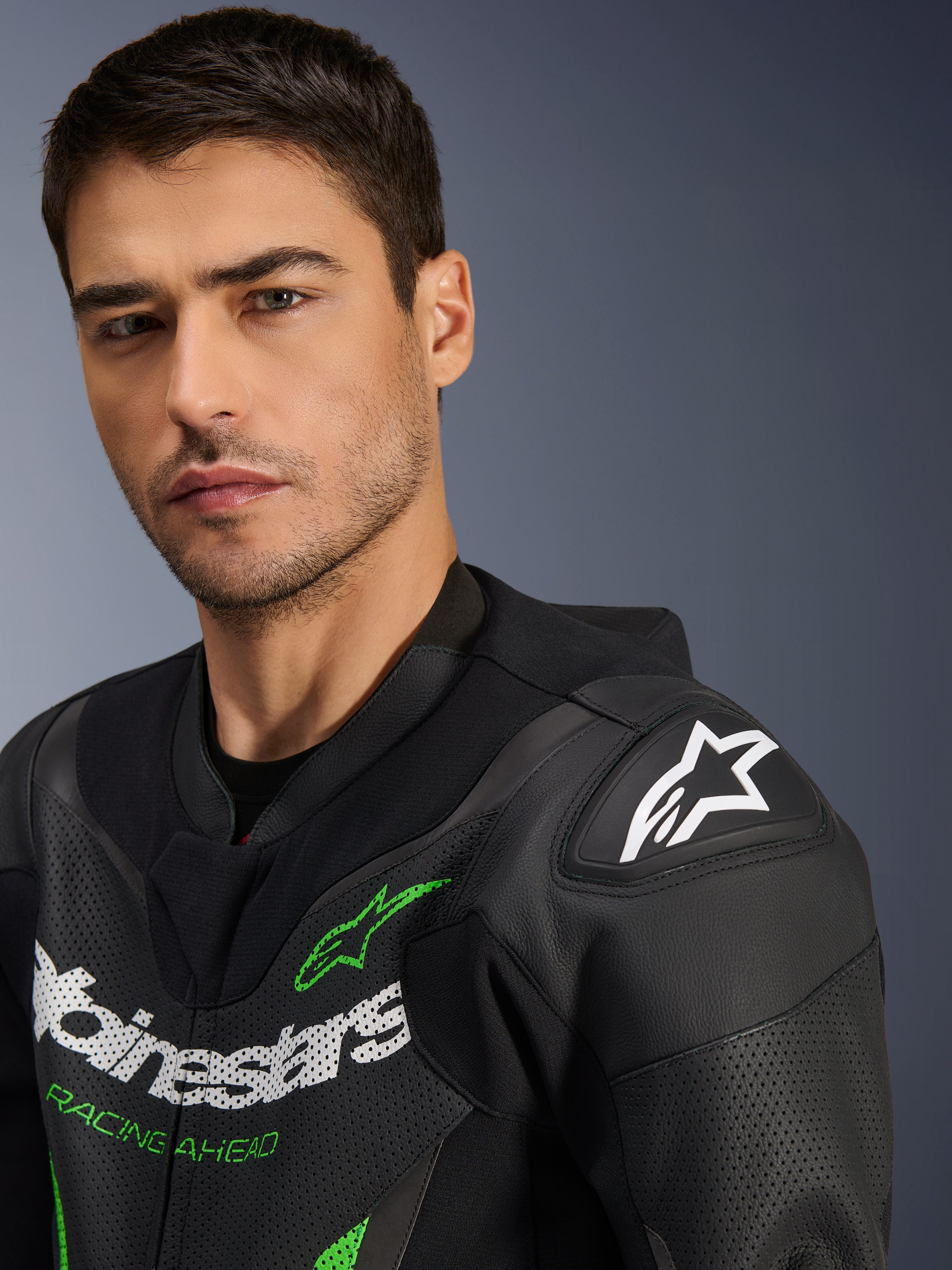 Alpinestars GP Force V2 Leather Suit - 1 Pieza, negro y verde, primer plano de un modelo masculino con el traje de carreras de motociclismo, con logotipos en blanco y verde, paneles de cuero perforado y protección de hombro DFS Lite con el logotipo de la estrella blanca.