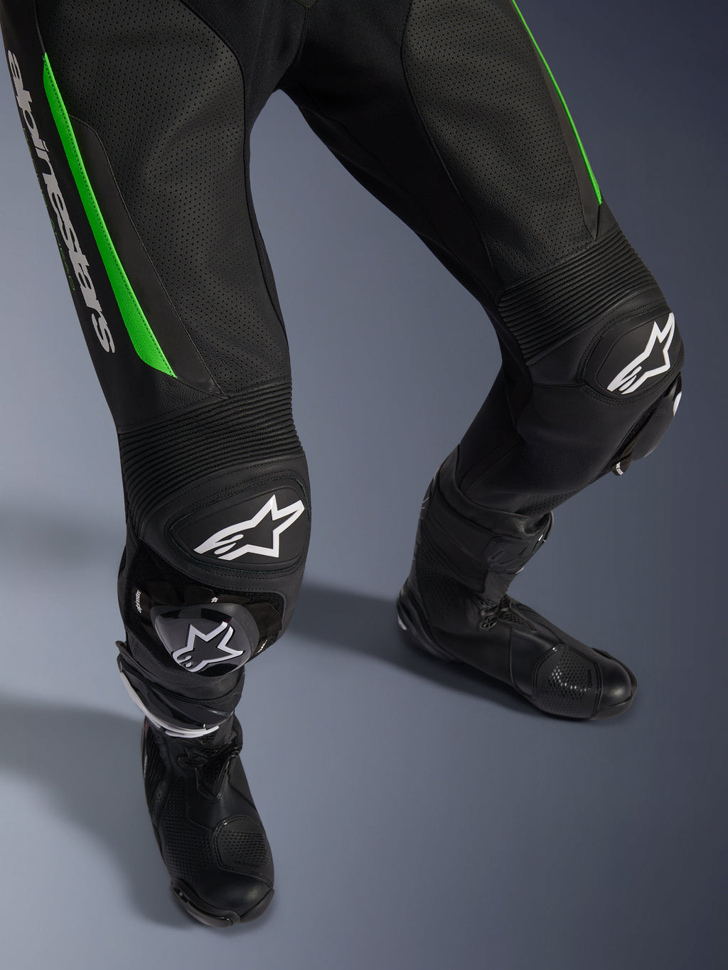 Alpinestars GP Force V2 Leather Suit - 1Piece, primer plano de las piernas en negro y verde, con construcción de cuero perforado, paneles elásticos de acordeón en las rodillas, logotipo de Alpinestars en blanco y deslizaderas de rodilla integradas, usado con botas de carrera negras