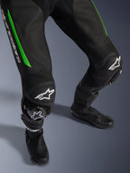 Alpinestars GP Force V2 Leather Suit - 1Piece, primer plano de las piernas en negro y verde, con construcción de cuero perforado, paneles elásticos de acordeón en las rodillas, logotipo de Alpinestars en blanco y deslizaderas de rodilla integradas, usado con botas de carrera negras