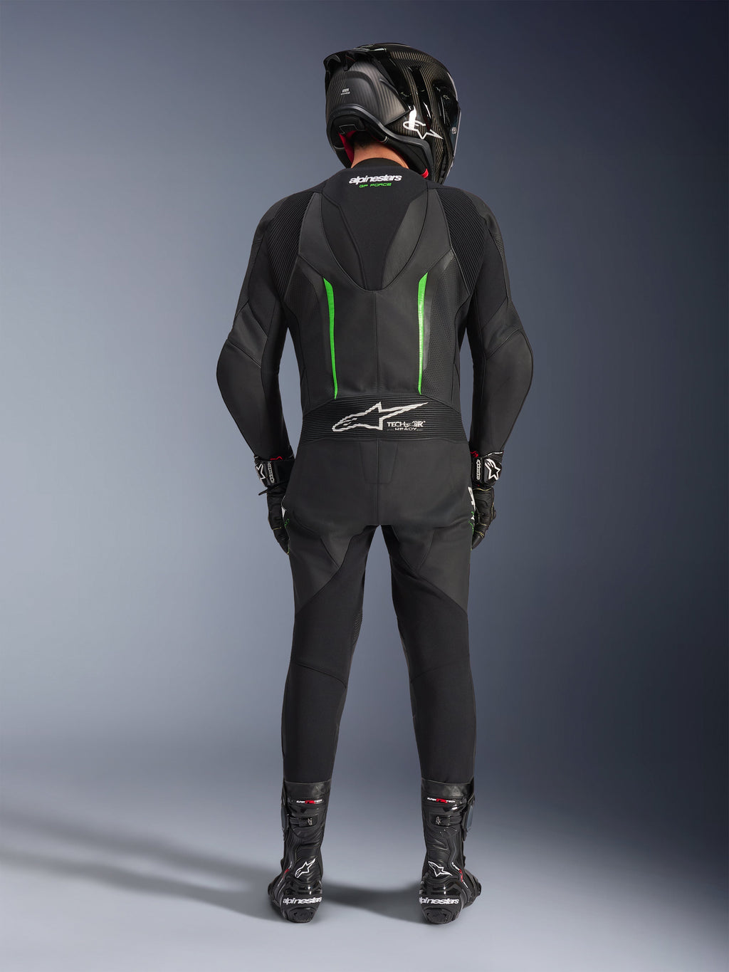 Piloto visto desde atrás con el traje de cuero de una pieza Alpinestars GP Force V2 en negro y verde, combinado con un casco de fibra de carbono negro, guantes de carreras negros y botas negras, con una joroba aerodinámica y el logotipo Tech-Air Ready.
