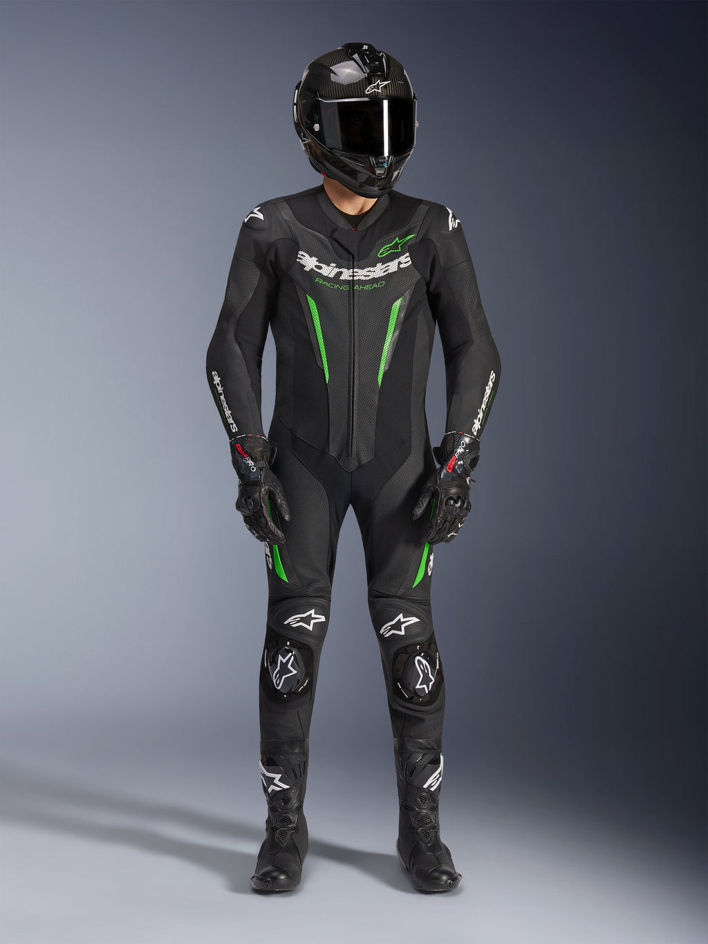 Piloto de motociclismo con el traje de cuero Alpinestars GP Force V2 de una pieza en negro y verde, combinado con un casco de fibra de carbono y guantes de carreras, con paneles de cuero perforados y logotipos blancos de Alpinestars, equipamiento profesional para pista y conducción deportiva