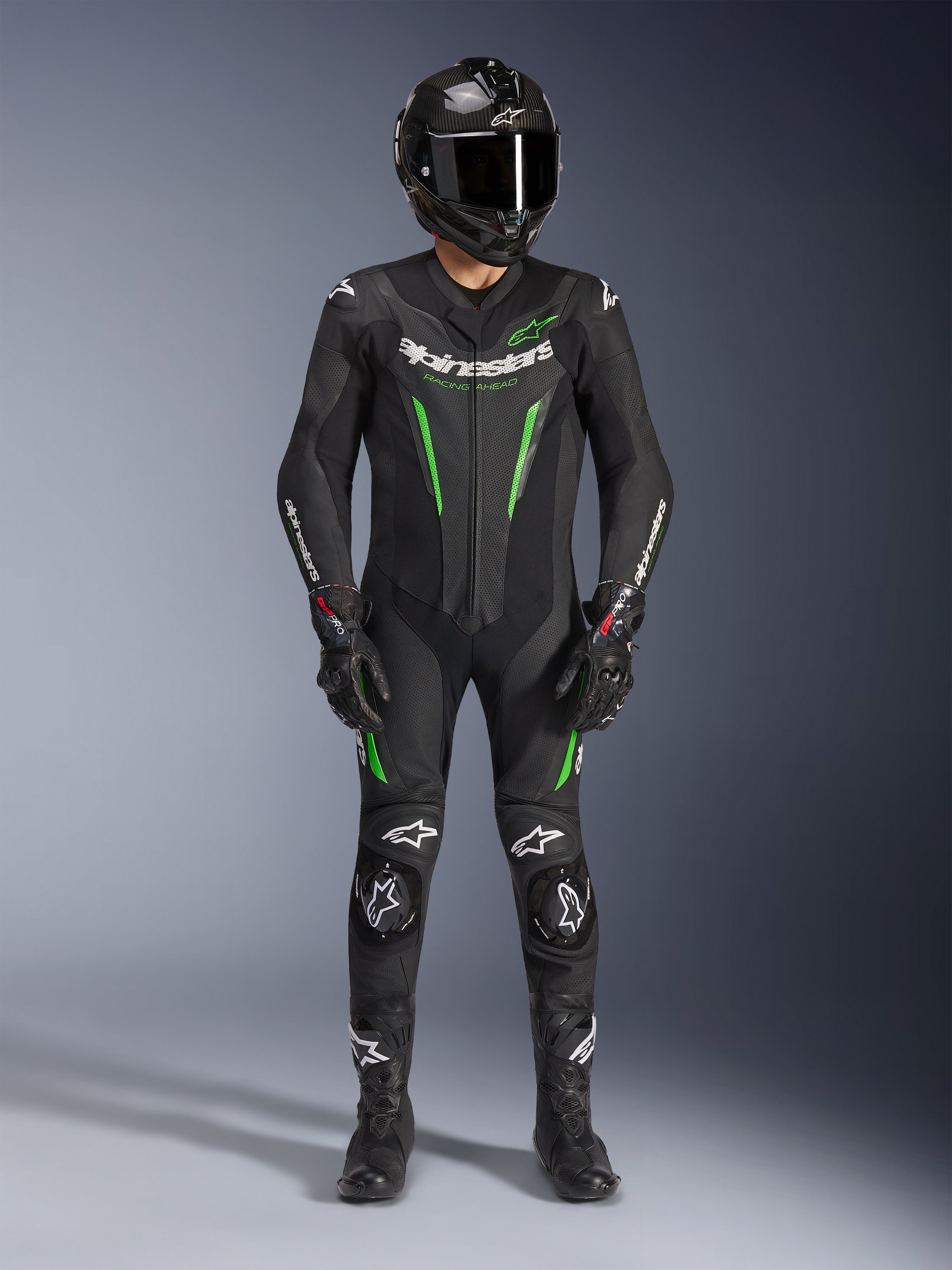 Piloto de motociclismo con el traje de cuero Alpinestars GP Force V2 de una pieza en negro y verde, combinado con un casco de fibra de carbono y guantes de carreras, con paneles de cuero perforados y logotipos blancos de Alpinestars, equipamiento profesional para pista y conducción deportiva