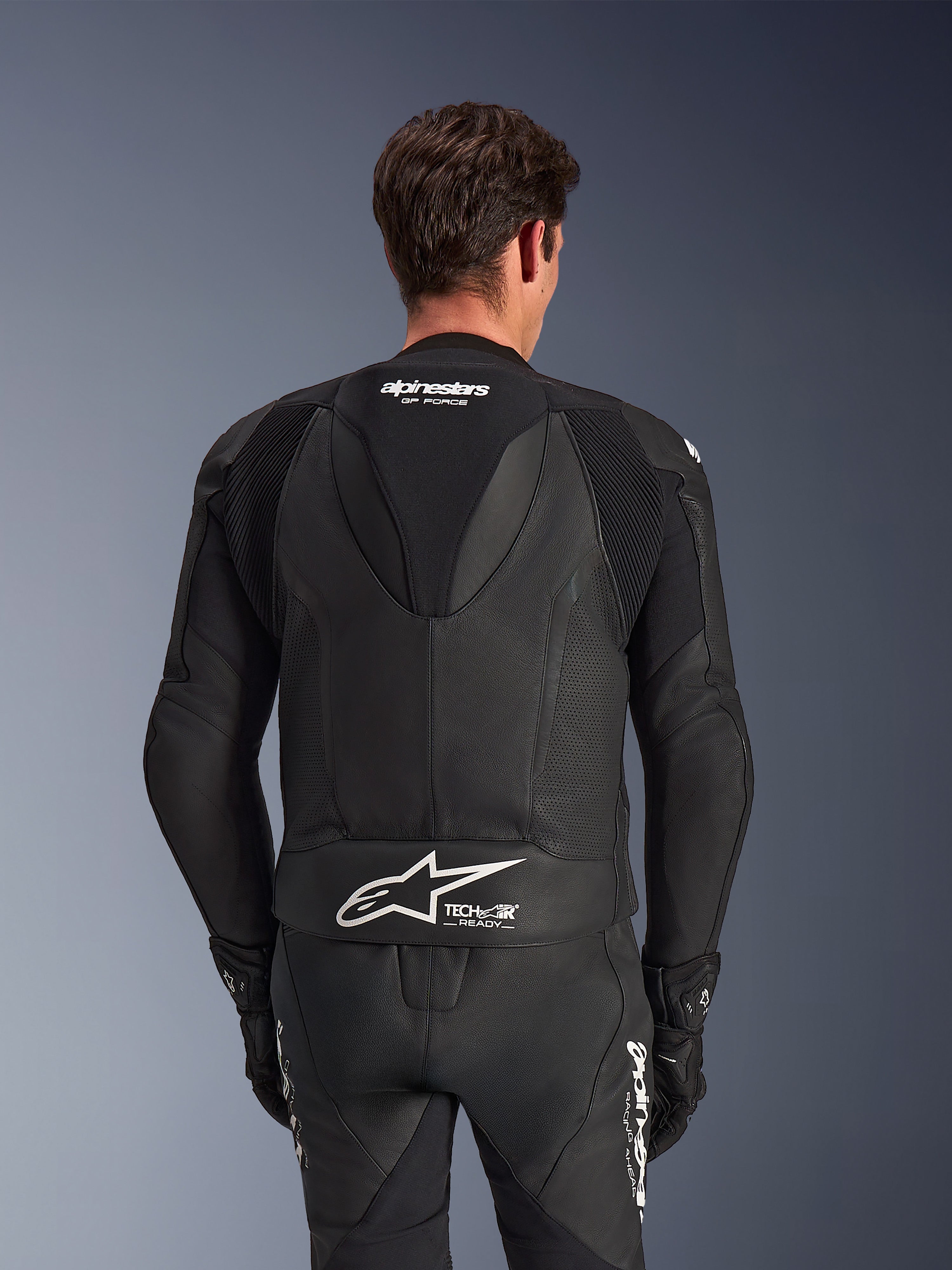 Alpinestars GP Force V2 Leather Suit- 2Piece, negro, vista trasera del piloto, con paneles de cuero perforado, joroba aerodinámica con marca GP Force y logotipo blanco de Alpinestars con el texto Tech-Air Ready en la parte inferior de la espalda.