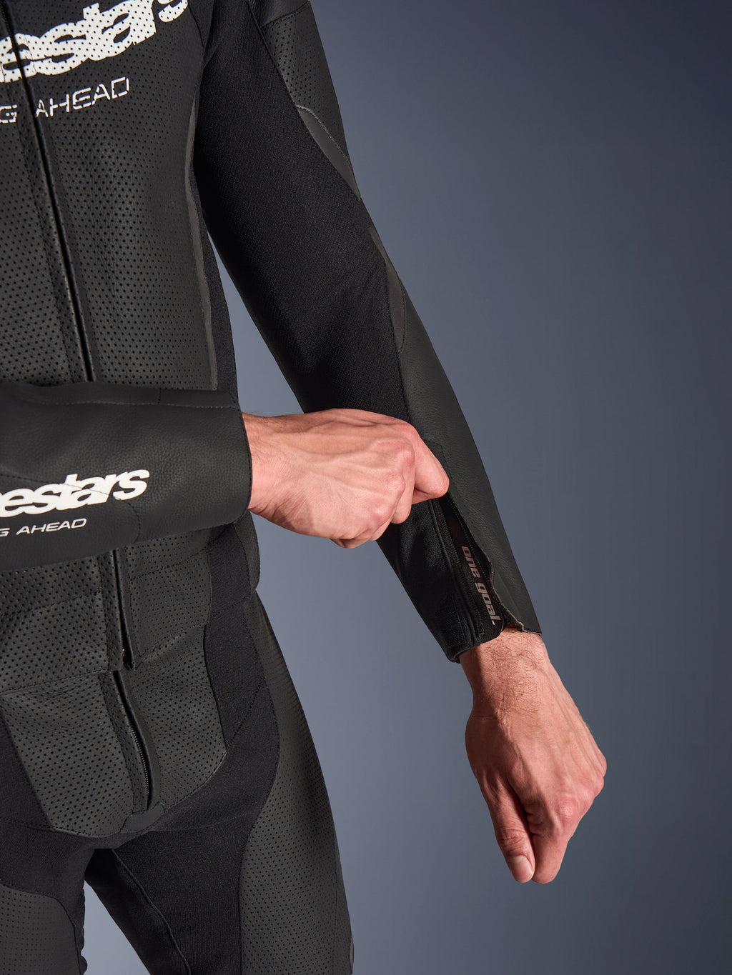 Alpinestars GP Force V2 2-Piece Leather Suit en negro, primer plano del ajuste de la abertura con cremallera en el antebrazo, con paneles de cuero perforado y construcción de tejido elástico.