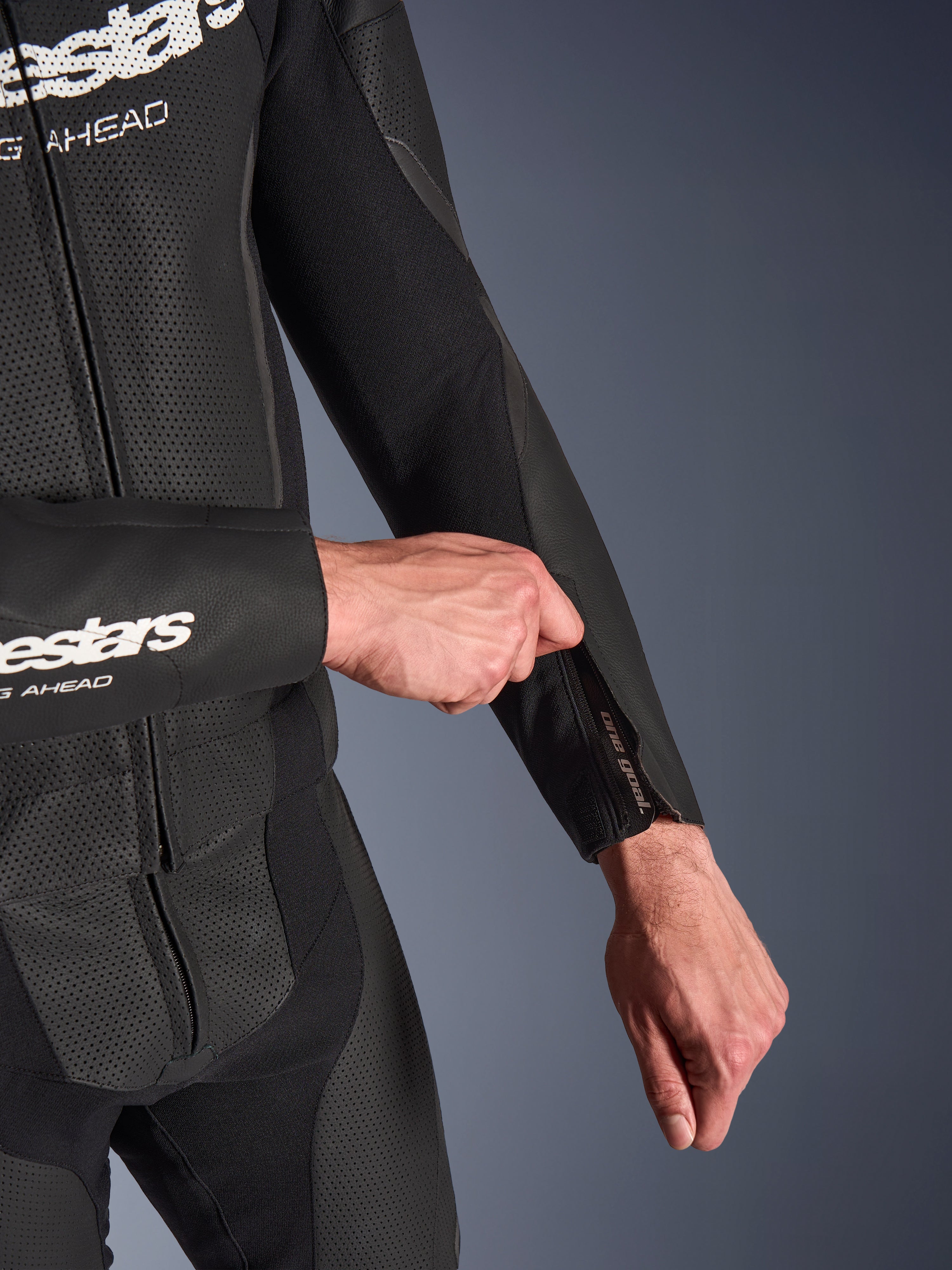 Alpinestars GP Force V2 2-Piece Leather Suit en negro, primer plano del ajuste de la abertura con cremallera en el antebrazo, con paneles de cuero perforado y construcción de tejido elástico.
