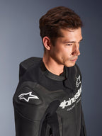 Traje de cuero de 2 piezas Alpinestars GP Force V2, negro, visto en un modelo, con el logo Astar blanco en el hombro, marca en el pecho, paneles de cuero perforado y joroba aerodinámica, equipamiento de carreras de motos de alto rendimiento