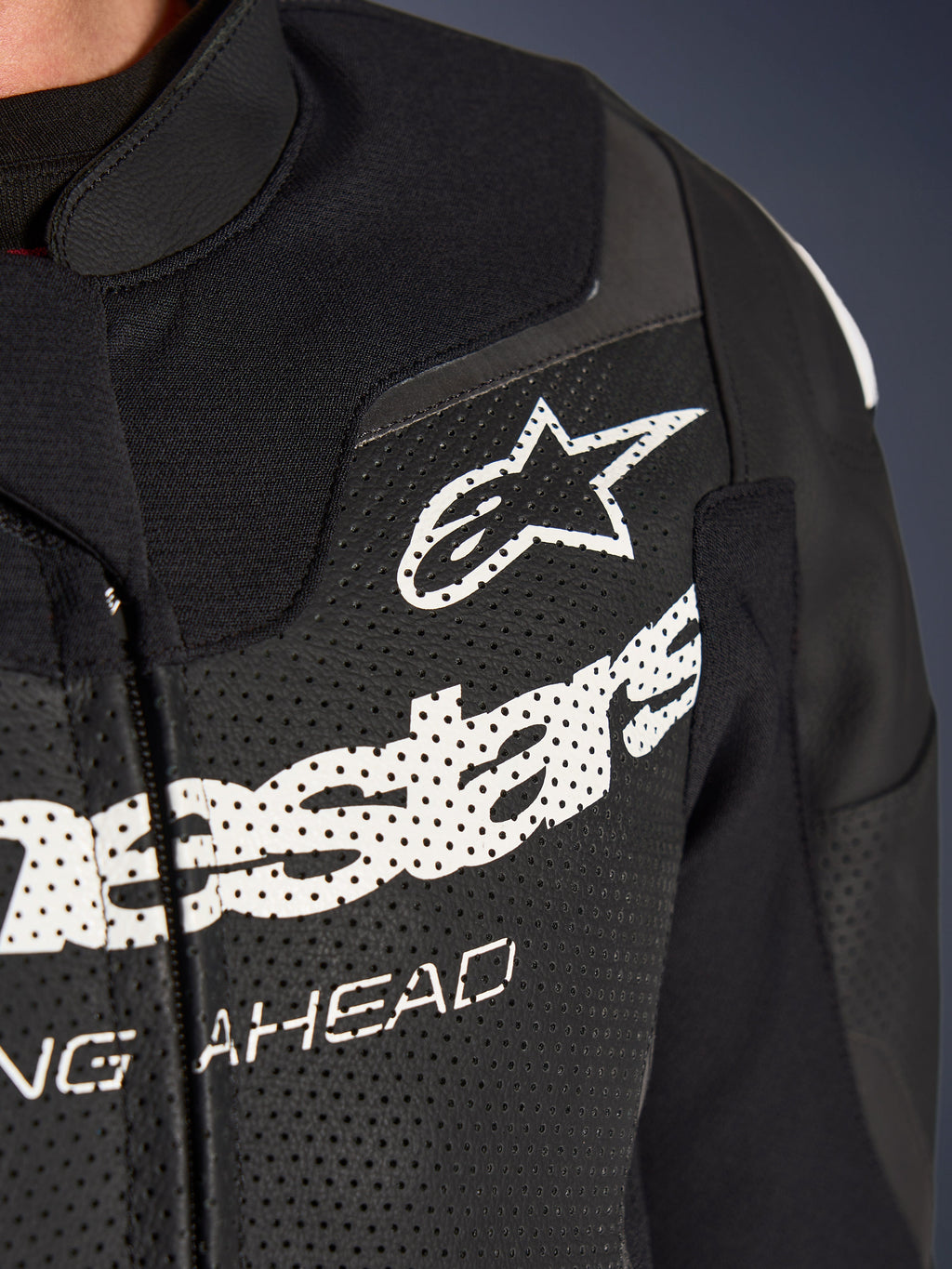 Traje de cuero de 2 piezas Alpinestars GP Force V2, traje de motociclismo de competición/deportivo, negro, primer plano del pecho de cuero perforado con logotipo y marca Alpinestars en blanco, resaltando los orificios de ventilación y la construcción texturizada.