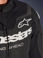 Traje de cuero de 2 piezas Alpinestars GP Force V2, traje de motociclismo de competición/deportivo, negro, primer plano del pecho de cuero perforado con logotipo y marca Alpinestars en blanco, resaltando los orificios de ventilación y la construcción texturizada.