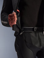 Traje de cuero de 2 piezas Alpinestars GP Force V2, negro, primer plano que muestra la cremallera de conexión de 360 grados en la cintura que une la chaqueta y el pantalón, con paneles de cuero bovino perforado y el logotipo de Alpinestars en blanco en la manga.