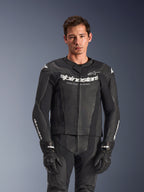 Traje de cuero Alpinestars GP Force V2 de 2 piezas, color negro, usado por un modelo, con paneles de cuero perforado y logotipo blanco 'Alpinestars Racing Ahead' en el pecho, combinado con guantes negros, equipamiento profesional para conducción deportiva